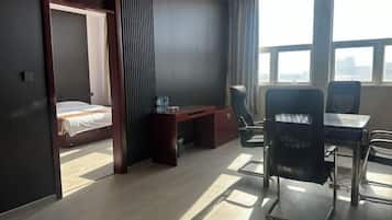 Een hotelkamer met een bed, bureau en stoelen. Grote ramen bieden uitzicht op de stad.