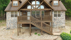 A two-story log cabin with a stone foundation, a wooden deck, and a staircase leading to the upper level. - 4 Master Suites! By StoneBridge Pool! SDC! (Branson West)