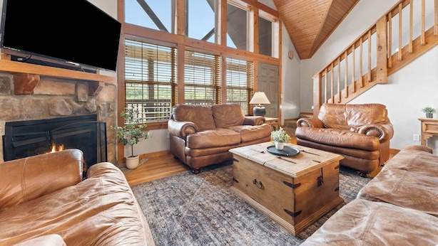 A spacious living room with leather sofas, a stone fireplace, large windows, and a wooden ceiling. - 4 Master Suites! By StoneBridge Pool! SDC! (Branson West)