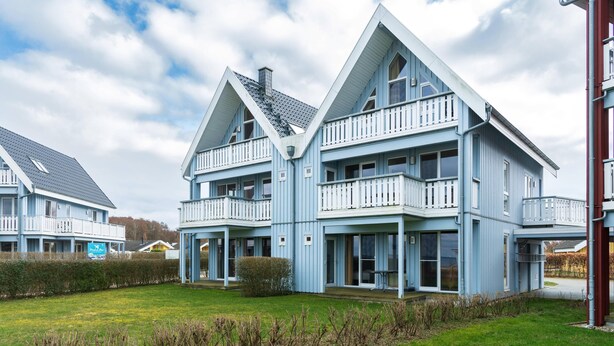 Ein geräumiges, hellblaues Haus mit zwei Etagen und einem Balkon in jeder Etage, umgeben von einem gepflegten Rasen und Hecken.