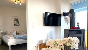 Ein Schlafzimmer mit einem Bett, einem an der Wand montierten Fernseher, einem Kamin und einer Blumenvase.