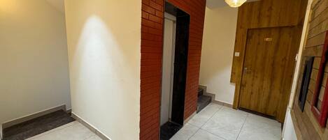 A hallway with a red brick wall, a wooden door, and a tiled floor.