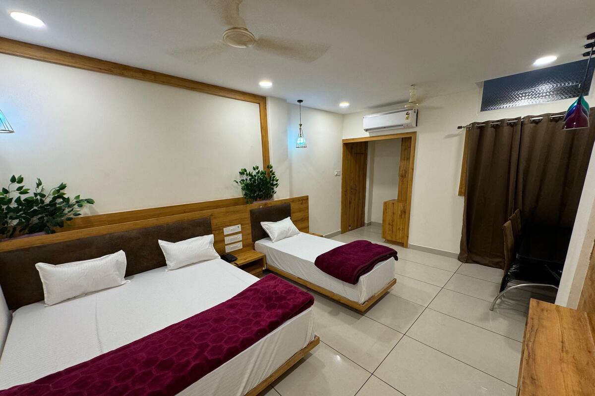 A hotel room with two beds, a ceiling fan, an air conditioning unit, a potted plant, and a view of the outside through a window.