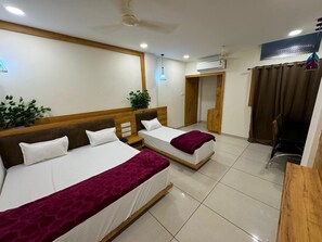 A hotel room with two beds, a ceiling fan, an air conditioning unit, a potted plant, and a view of the outside through a window. - Hotel My Budget (Ujjain)