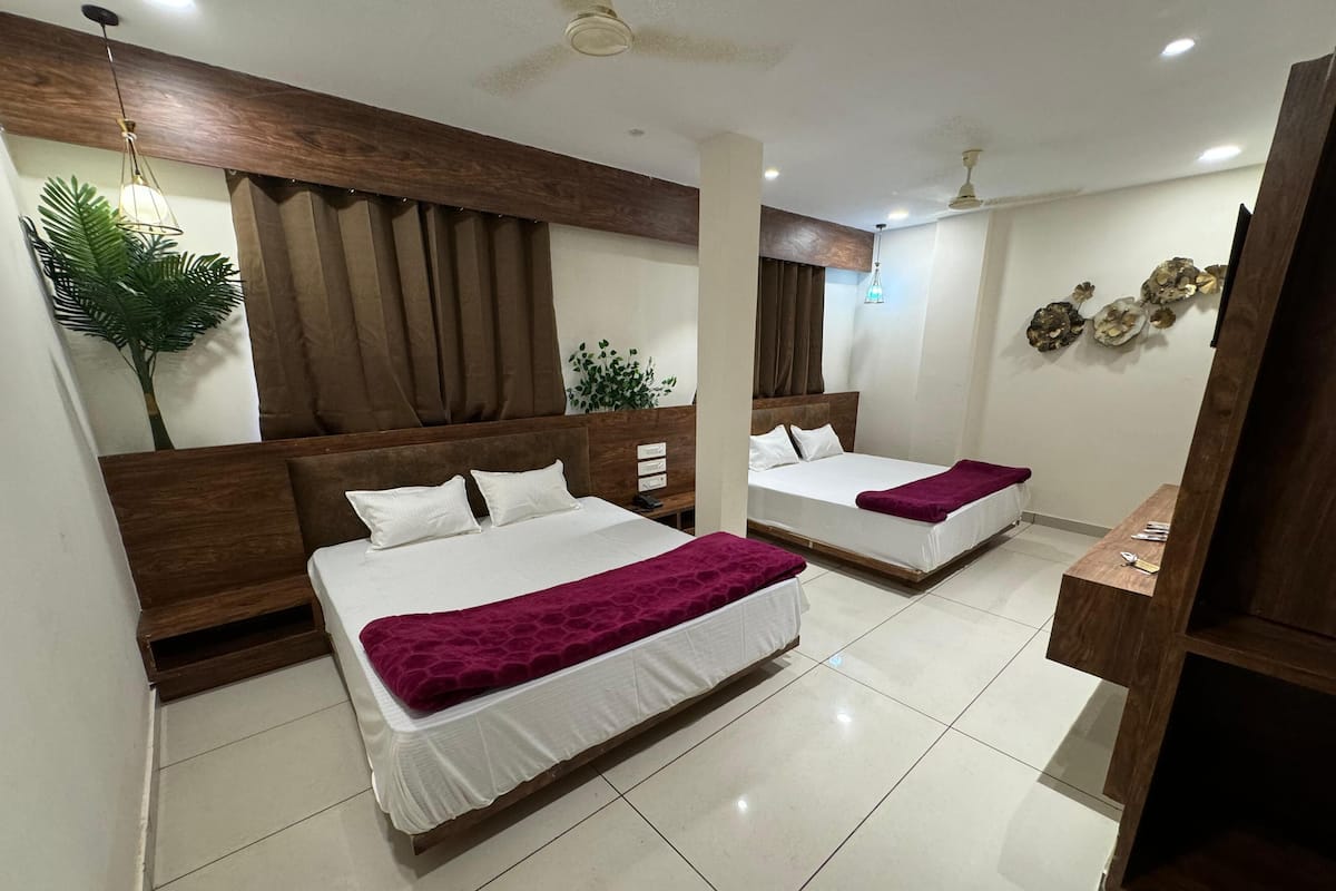 A hotel room with two beds, a wooden headboard, a large potted plant, and a ceiling fan.