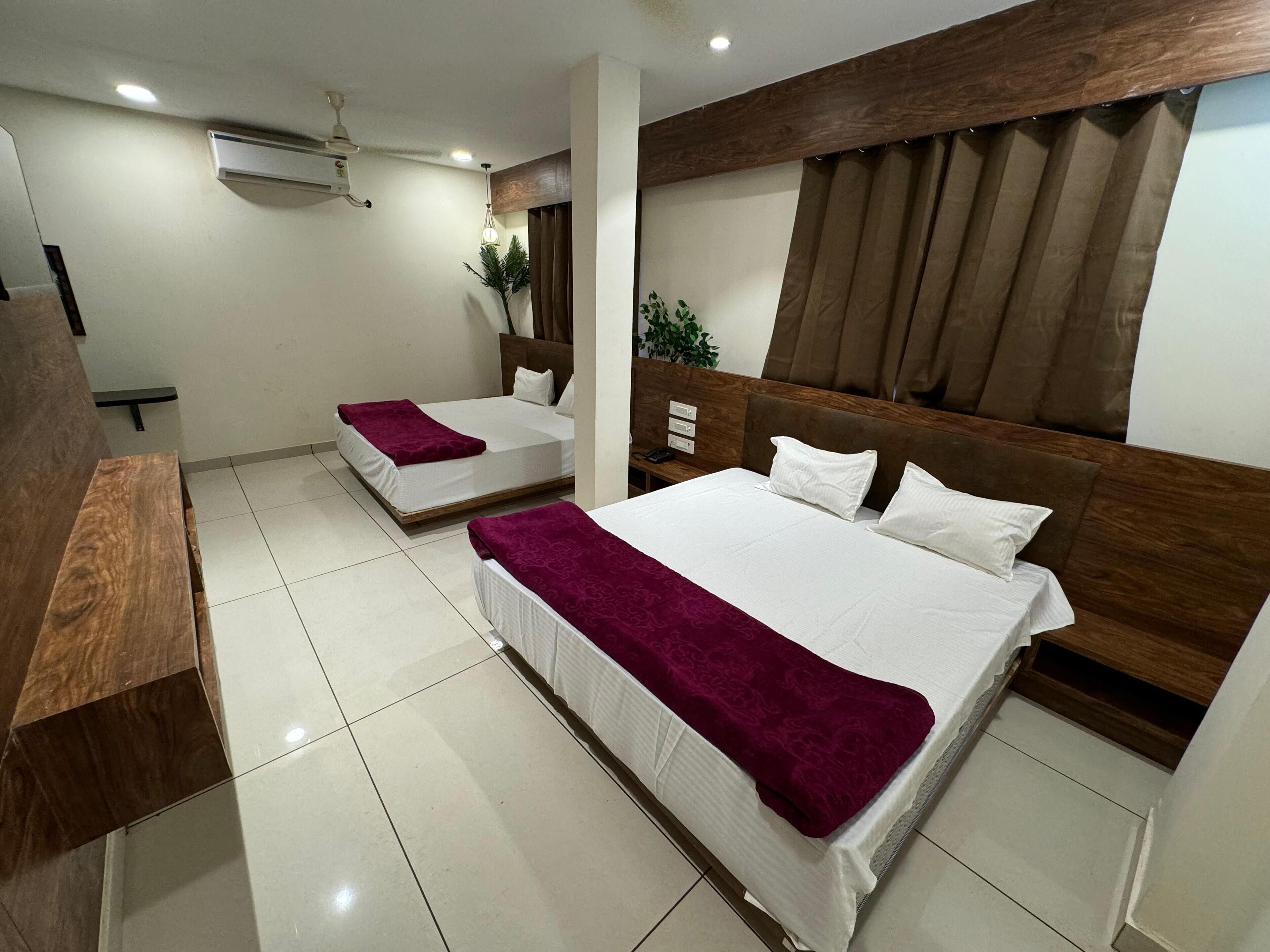Ein Hotelzimmer mit zwei Betten, einem Holzkopfteil, einem Deckenventilator, einer Klimaanlage und einem kleinen Nachttisch mit Lampe.