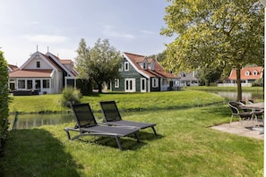 A serene lakeside setting with a grassy lawn, two lounge chairs, and a small table.