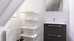 Een moderne badkamer met witte betegelde wanden, een witte radiator, een donker houten kastje met spiegel erboven en een witte plank.