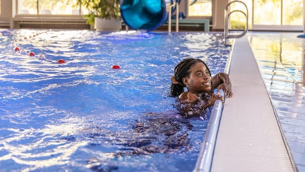 A swimming pool with a person in the water, a blue cylindrical object, and a plant in the background.
