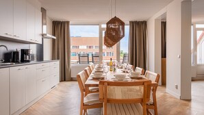 Una cocina moderna con armarios blancos, una cafetera negra y un comedor con una mesa de madera dispuesta para seis.