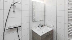 A modern bathroom with white tiles, a shower, a sink, and a mirror.