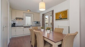 Une cuisine compacte avec des meubles blancs, un four à micro-ondes et un coin repas comprenant des chaises en osier et une table en bois.