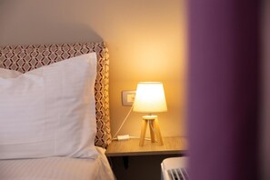 Un lit bien fait, avec une tête de lit décorée, une table de chevet avec une lampe et une prise électrique.