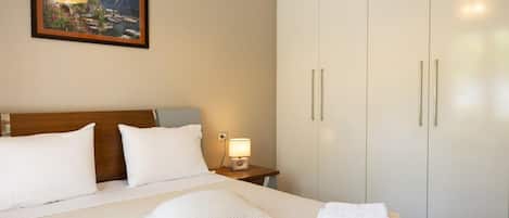 A hotel room with a large bed, a nightstand with a lamp, a wardrobe, and a framed picture on the wall.