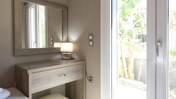 Une salle de bain avec un meuble-lavabo en bois, un miroir, une lampe de chevet et une vue sur un jardin, visible à travers une porte vitrée.