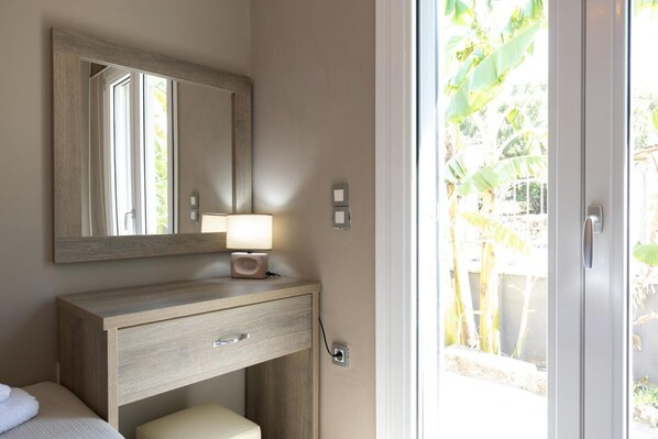 Une salle de bain avec un meuble-lavabo en bois, un miroir, une lampe de chevet et une vue sur un jardin, visible à travers une porte vitrée.