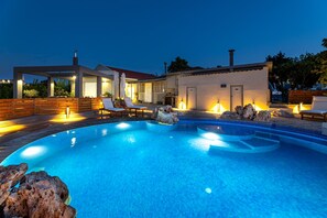 Une piscine dotée de chaises longues et d’un espace patio, le tout entouré d’une maison avec un toit en tuiles et des éléments d écoratifs en pierre.