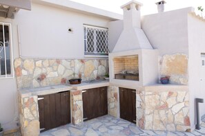 An outdoor kitchen area with stone walls, wooden cabinets, and a brick oven. - Tselepis Villa at Lakithra (Kefalonia)