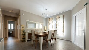 Un espace repas avec une table et des chaises en bois, un lustre et une vue sur les bâtiments à travers de grandes fenêtres.