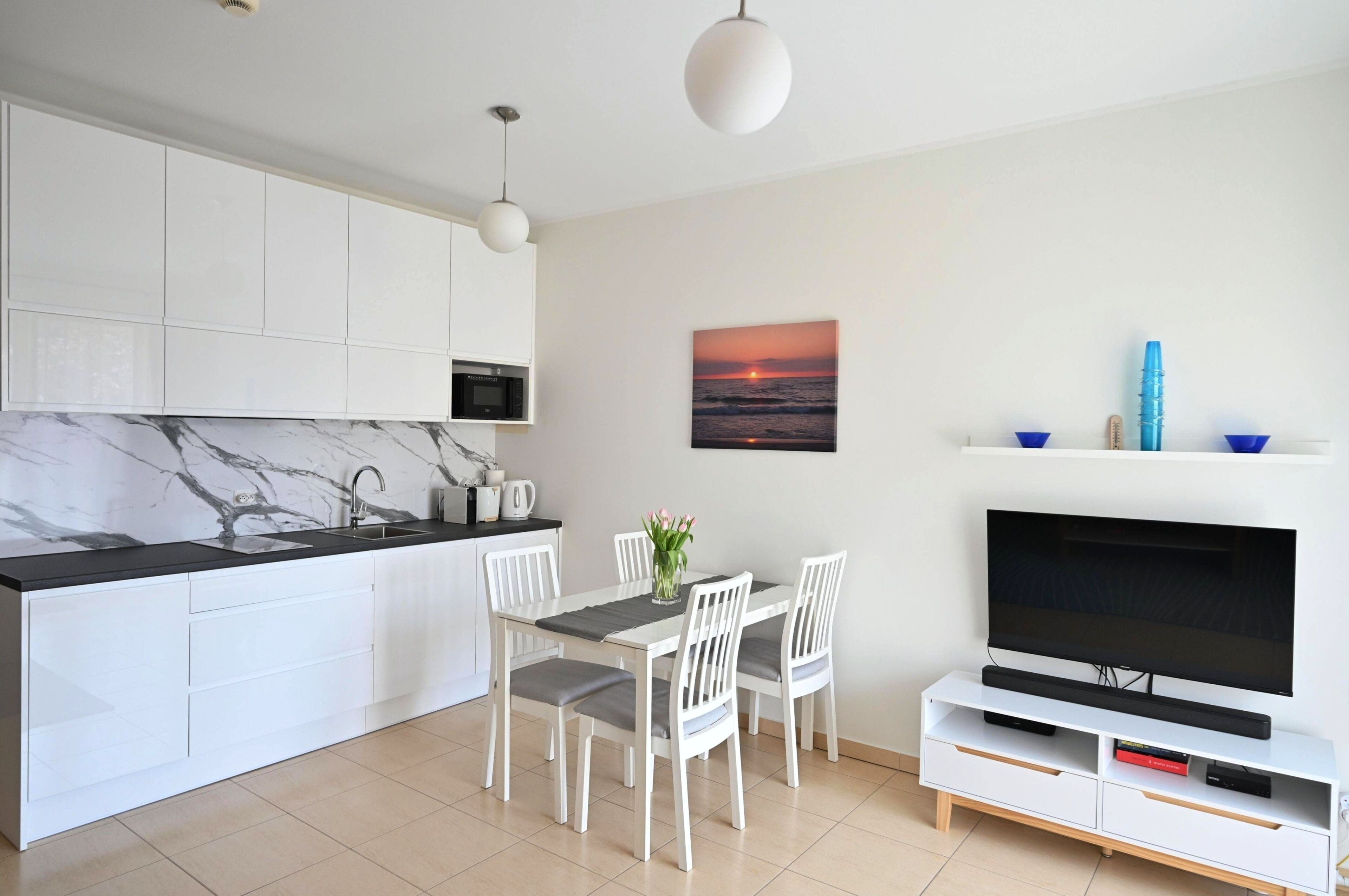 A modern kitchen with white cabinets, a marble backsplash, and a dining area with a white table and chairs.