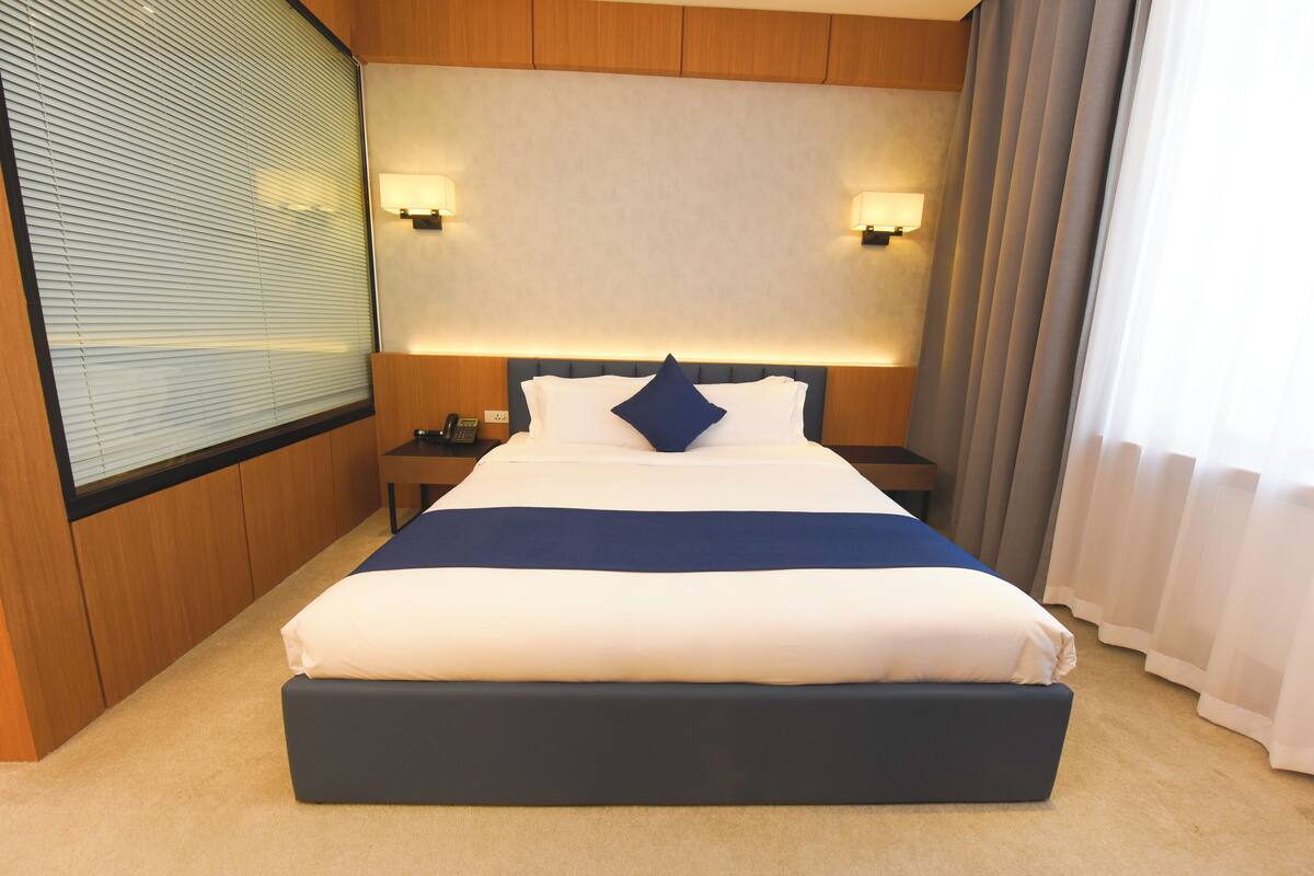 A hotel room with a large bed, a bedside table, a telephone, and a wall-mounted light fixture.