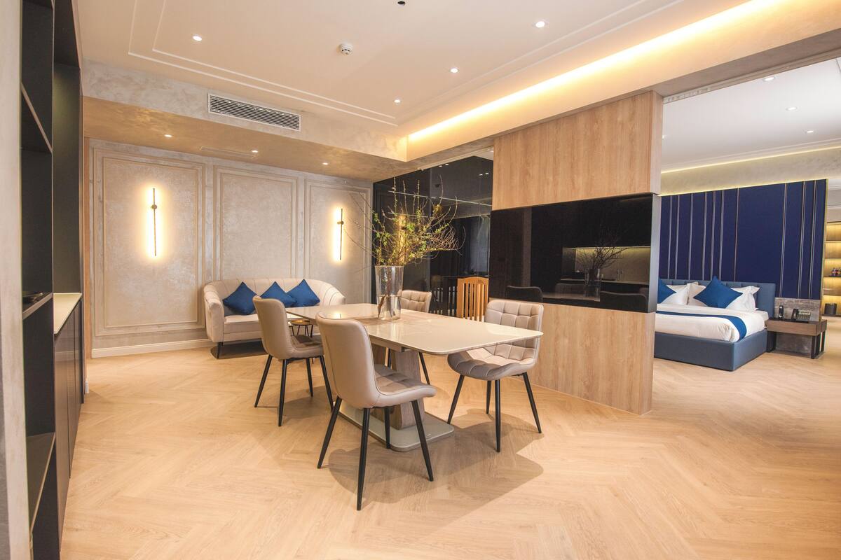 A modern hotel room with a dining area, a sofa, a bed, and a large window.