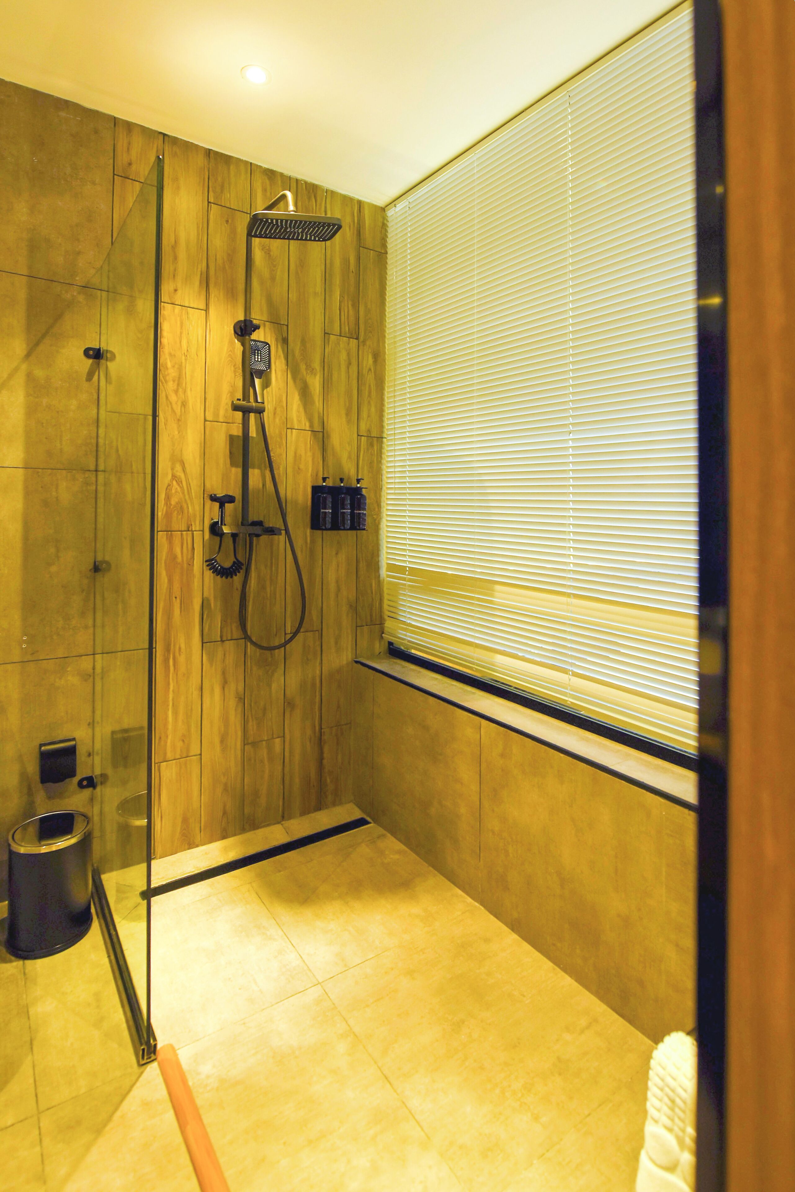 Une douche moderne dotée d’une porte en verre, de murs recouverts de panneaux en bois et d’une fenêtre avec des stores.
