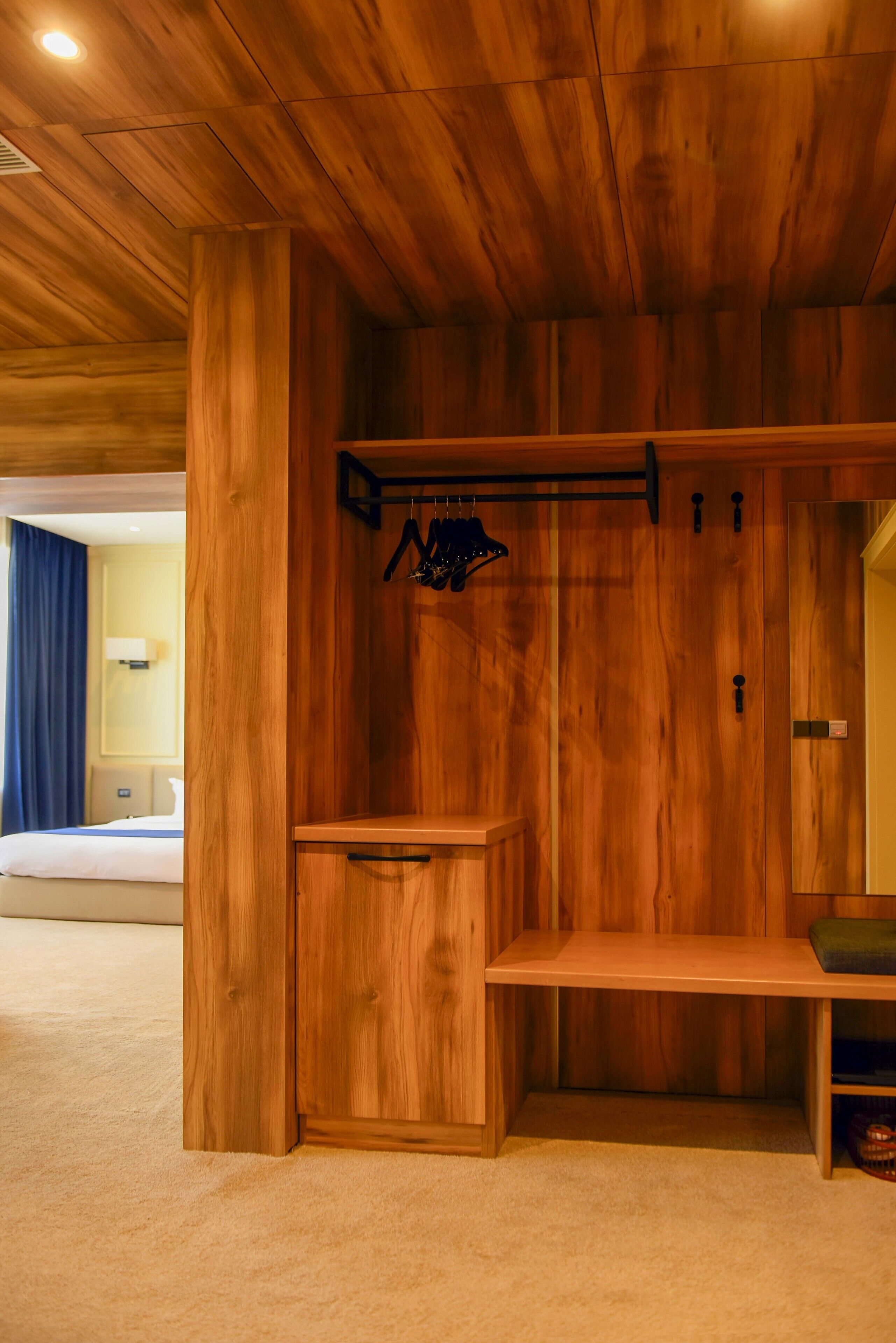 Una habitación de madera con una cama, un banco y un perchero.