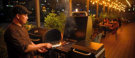 A person grilling outdoors at night with string lights overhead.