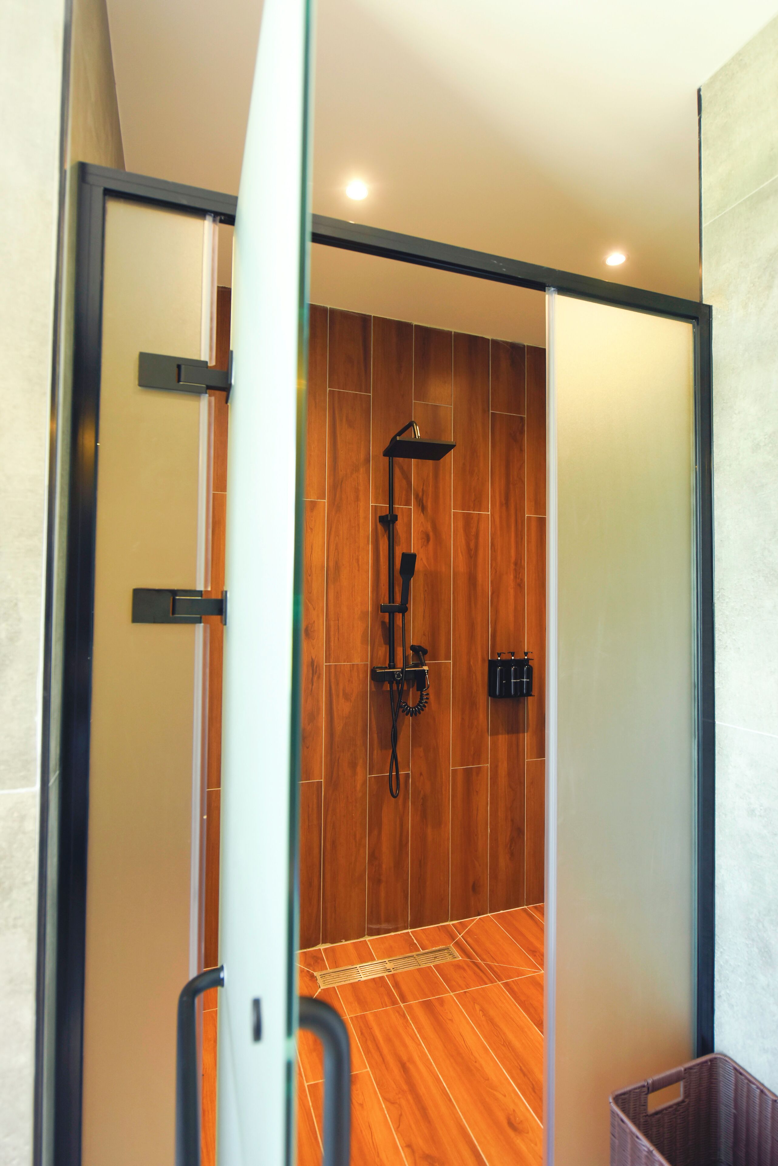A modern bathroom with a wooden floor, a glass shower enclosure, and a black towel rack.