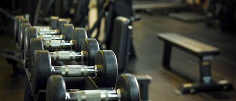A row of dumbbells in a gym with benches and other fitness equipment in the background.