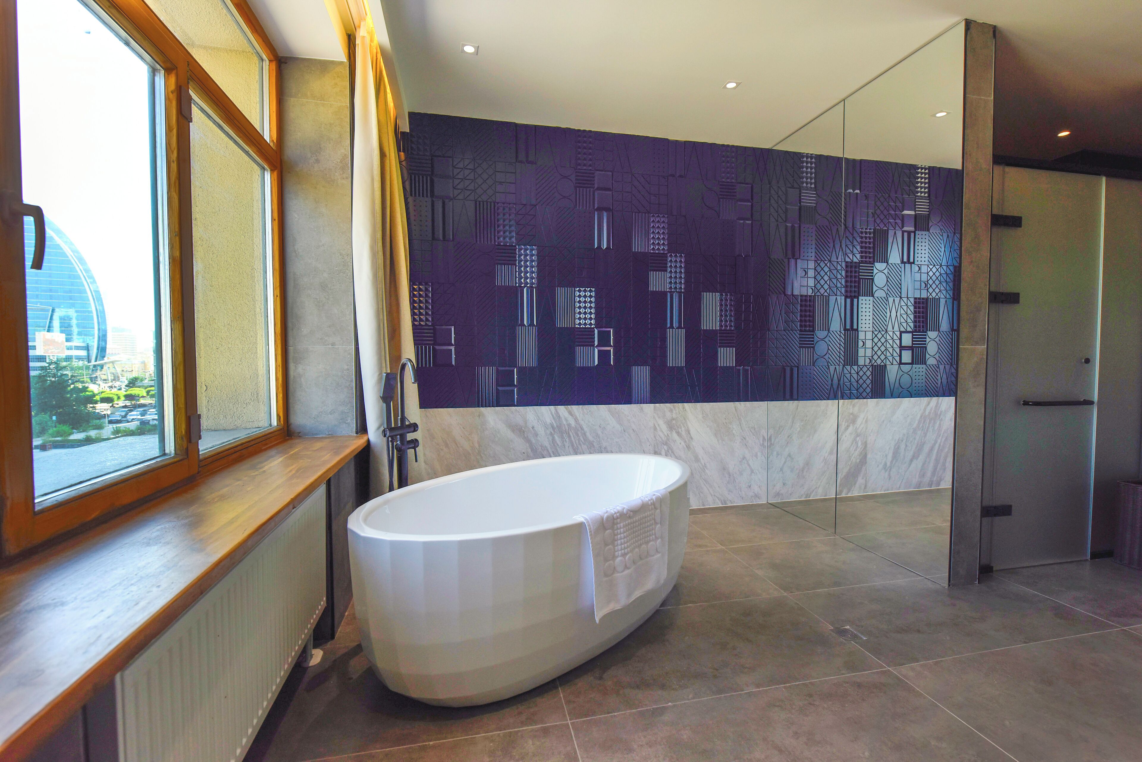 A modern bathroom with a freestanding bathtub, a large window, and a patterned wall.