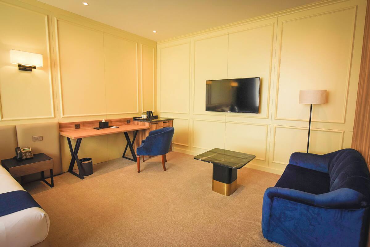 A hotel room with a bed, a desk, two chairs, a TV, and a lamp.