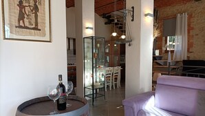 A living room with a purple sofa, a wooden barrel with wine bottles, and a dining area with a glass cabinet and chairs. - Open space studio apartment with patio near Siena (Monteriggioni)