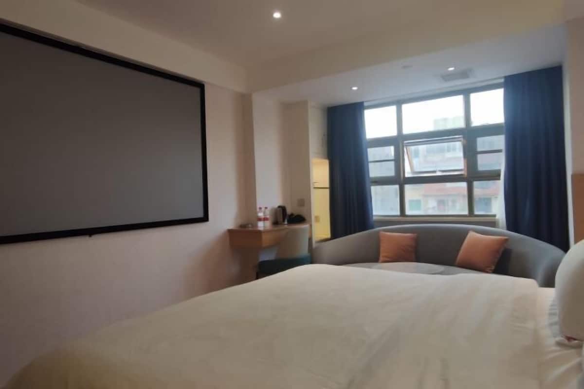 Une chambre d’hôtel équipée d’un lit, d’un bureau, d’une chaise, d’une fenêtre avec des rideaux et d’un écran de projection.