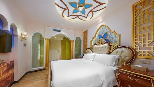 Une chambre à coucher avec un grand lit, une tête de lit décorative et un téléviseur fixé au mur.