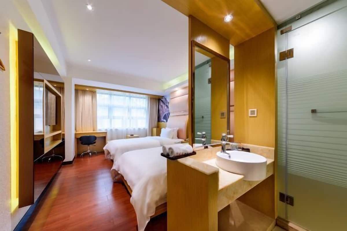 Une chambre d’hôtel avec deux lits, un bureau, un grand miroir et une salle de bain équipée d’un lavabo et d’une douche.