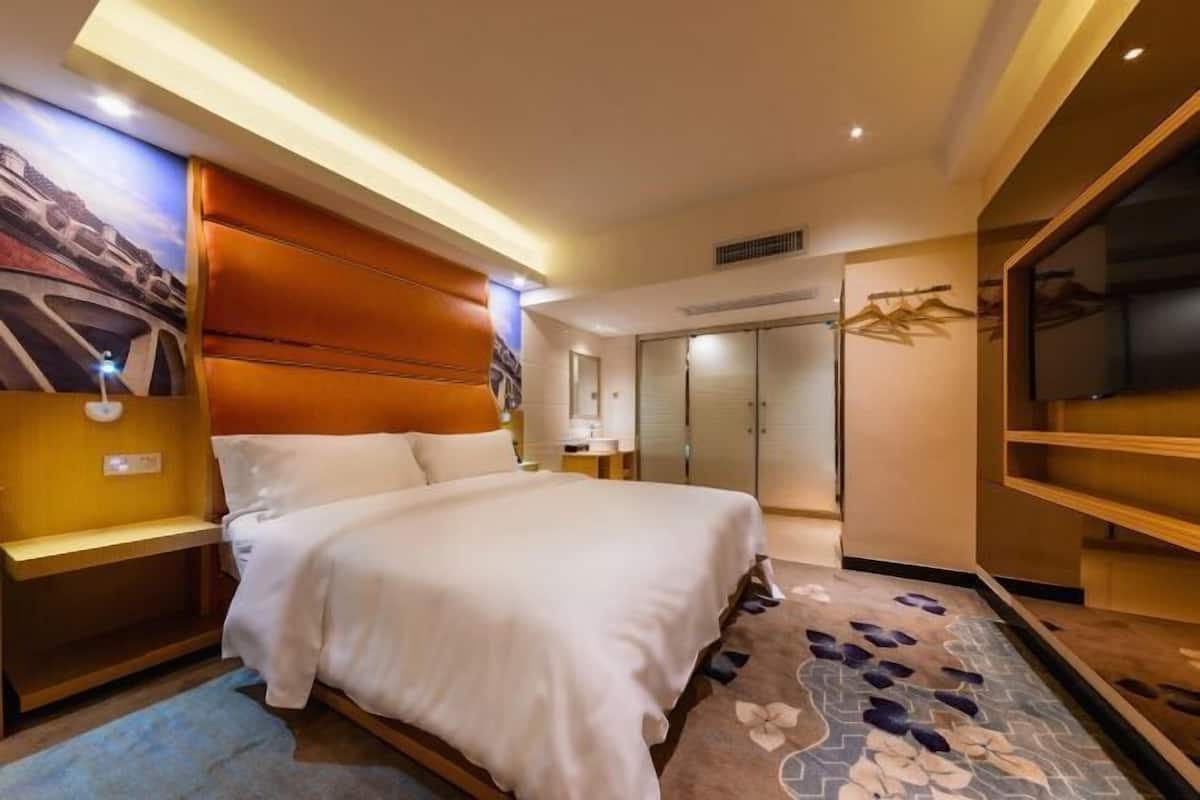 Une chambre d’hôtel comprenant un lit, des tables de chevet, un téléviseur, une armoire et un tapis à motifs floraux.