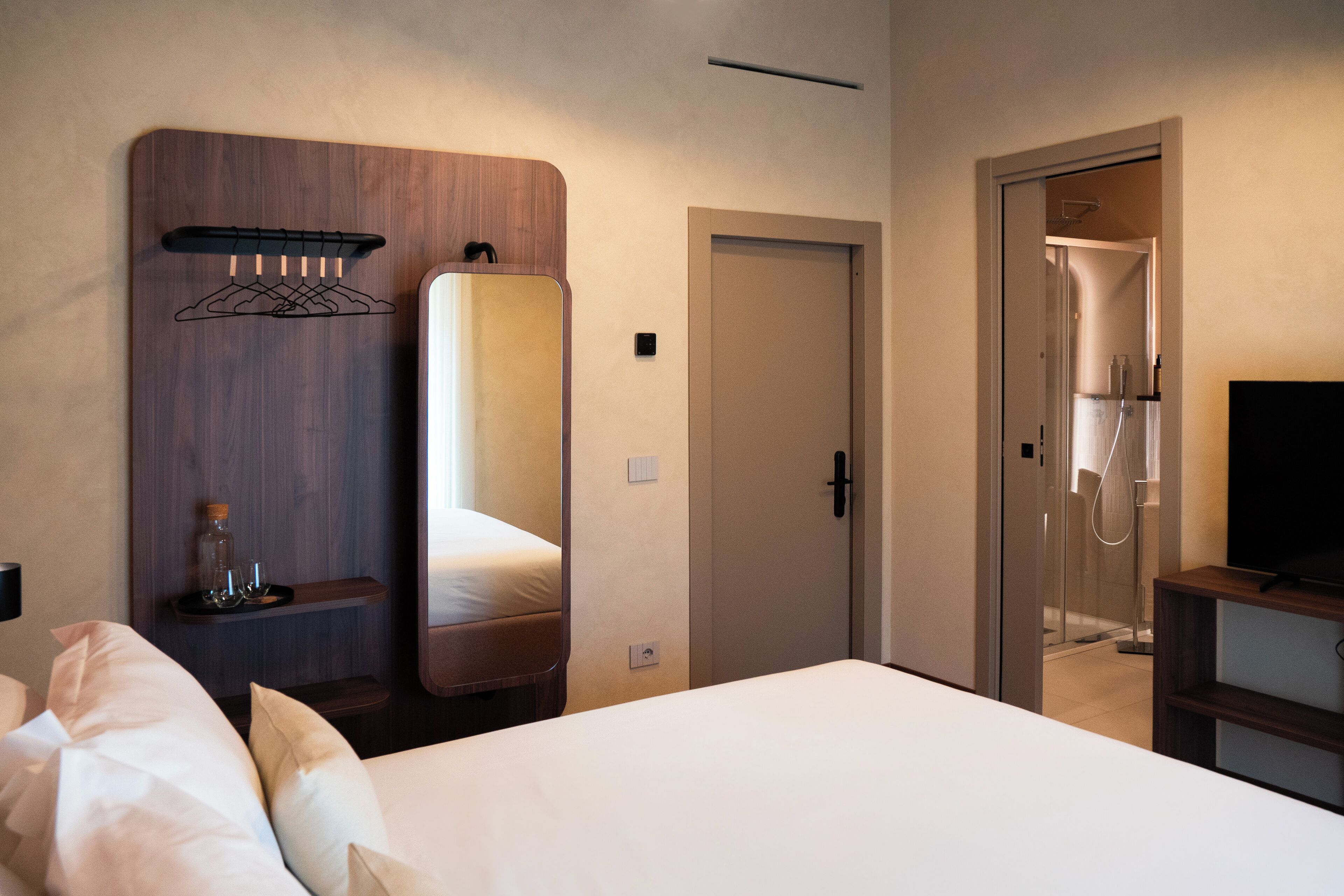 Habitación de hotel con una cama grande, cabecera de madera, un espejo, un televisor y zona de ducha.