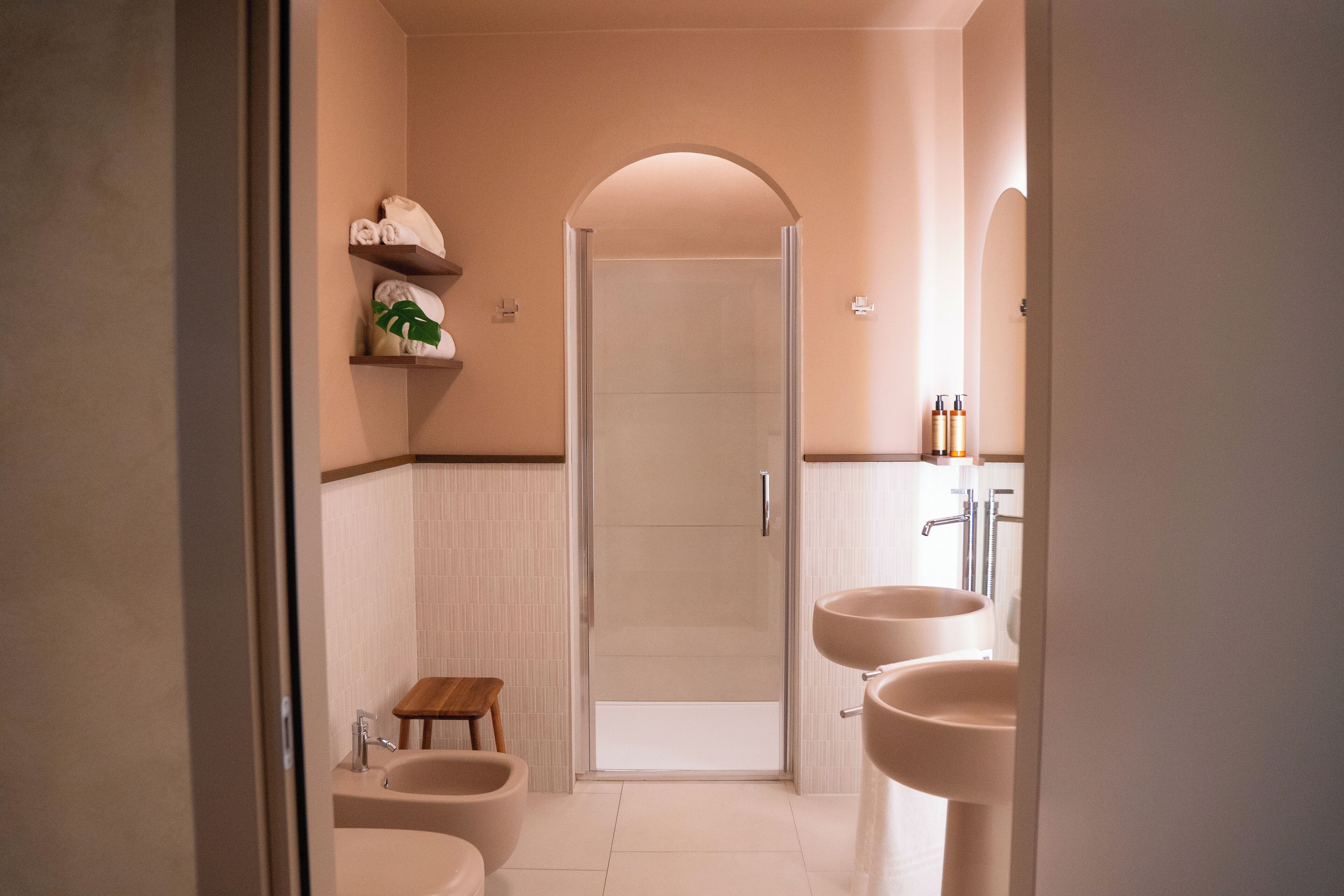 Un bagno moderno con doccia, due lavabi, un water e un piccolo sgabello di legno.