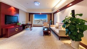 A hotel room with a large TV, a sofa, a coffee table, a plant, and a view of a cityscape. - Huatian Hotel(Wuhan Xudong Metro Station) (Wuhan)