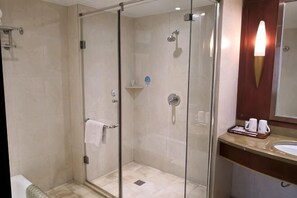 Eine Duschkabine mit Glastüren, ein Handtuchhalter, ein Waschbecken mit Spiegel und eine Ablage mit Toilettenartikeln.