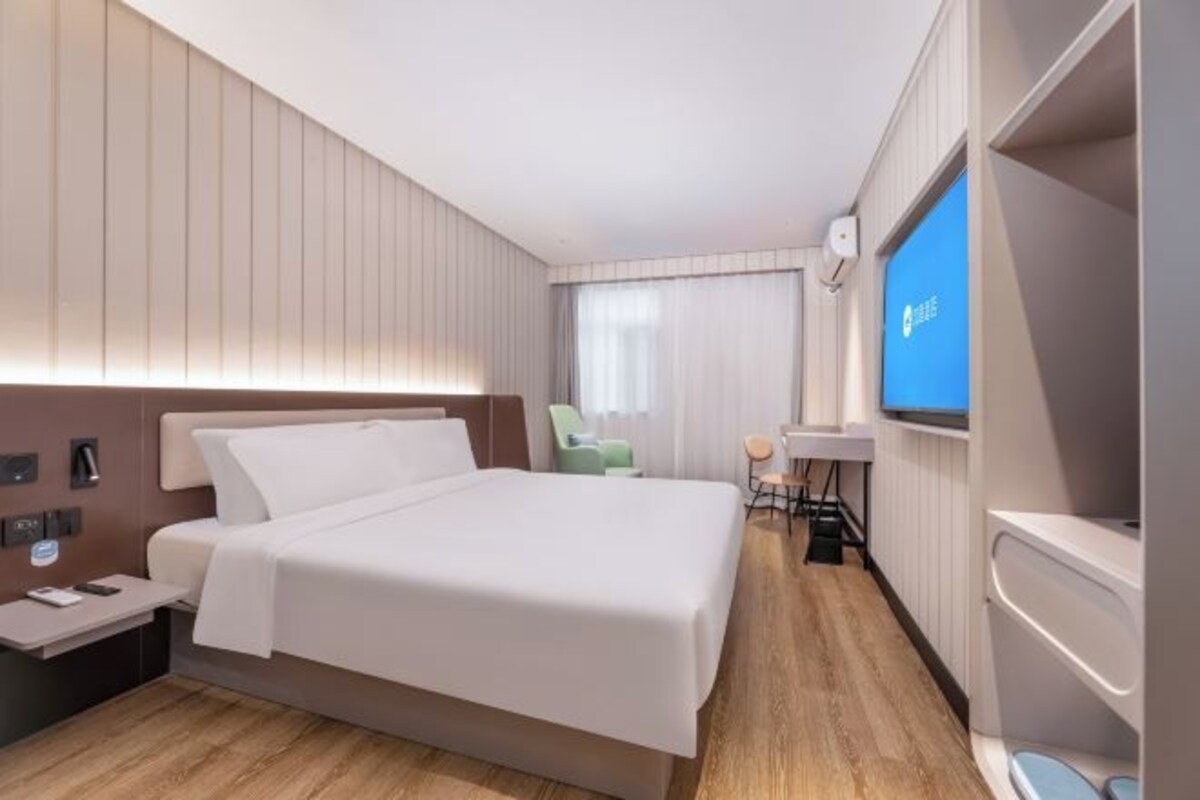 Ein modernes Hotelzimmer mit Bett, Nachttisch, Fernseher und einer kleinen Sitzecke.