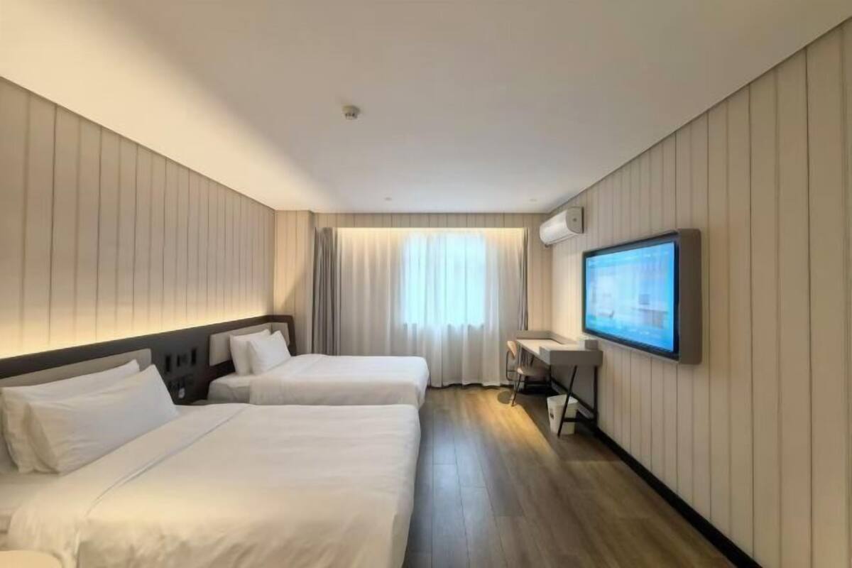 A hotel room with two beds, a desk, a TV, and a window with curtains.