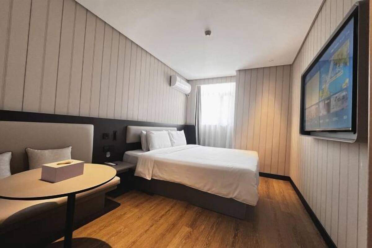 A hotel room with a bed, a small table, a sofa, and a TV mounted on the wall.