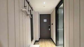 A narrow hallway with a wooden floor, a door with a handle, and a small bench. - HanTing Hotel (Zhangjiagang Jingang RT-MART Branch) (Zhangjiagang)