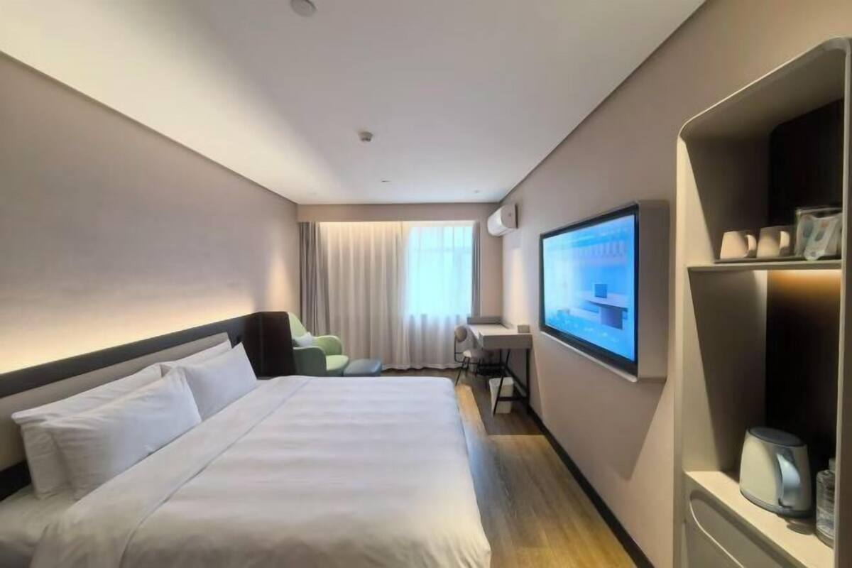 A hotel room with a bed, a desk, a TV, and a shelf with items.