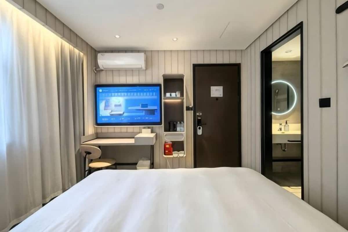 A hotel room with a bed, a desk with a computer, a TV, a door, and a bathroom.