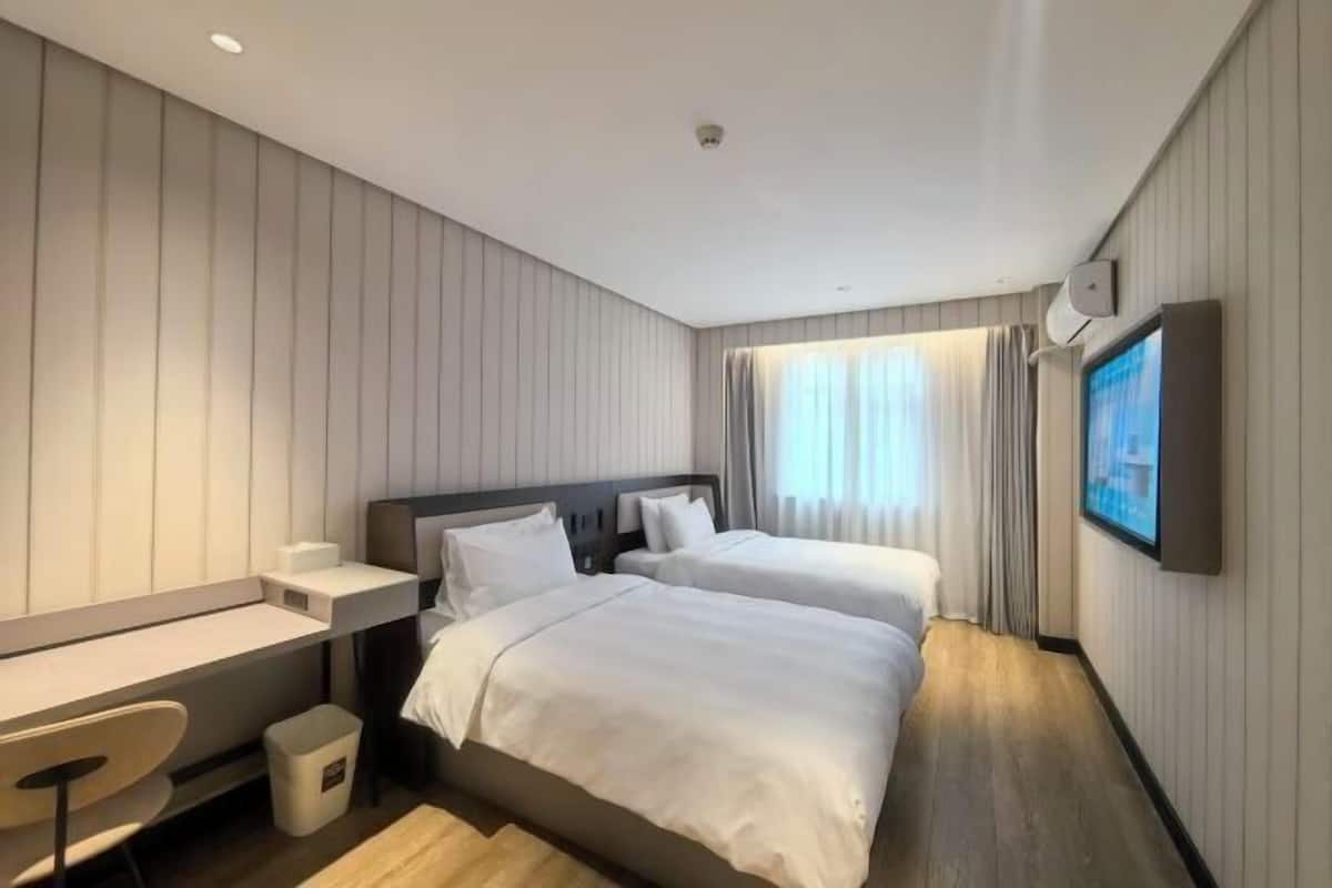 A hotel room with two beds, a desk, a chair, a TV, and a window with curtains.