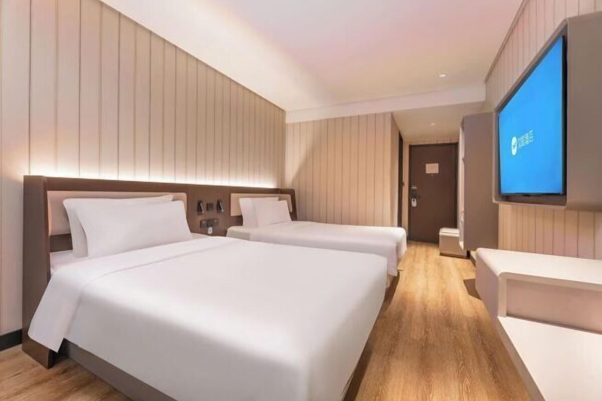 A modern hotel room with two beds, a TV, and a wooden floor.